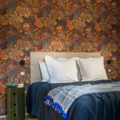 Chambre à coucher avec papier peint floral coloré, lit double bleu et tête de lit beige.