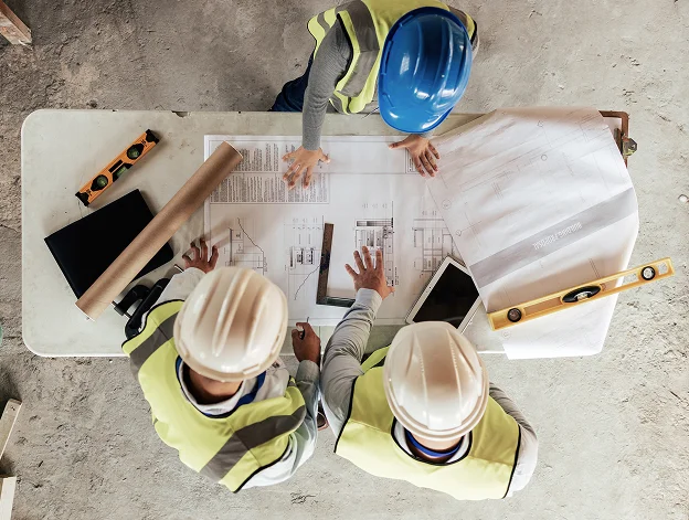 Trois constructeurs en casque regardent des plans sur une table de chantier à l'Ile de Ré en Charente-Maritime 17