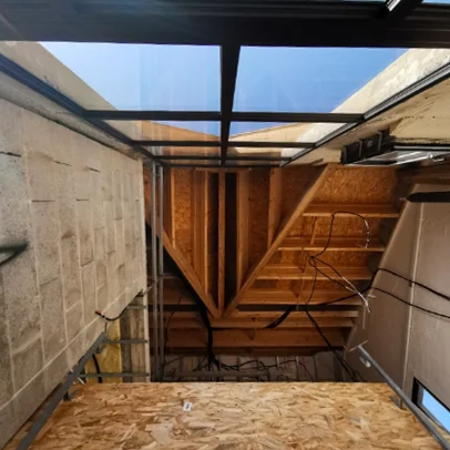 Un intérieur en construction avec des murs en blocs, un plancher en OSB et un plafond en bois et verre.