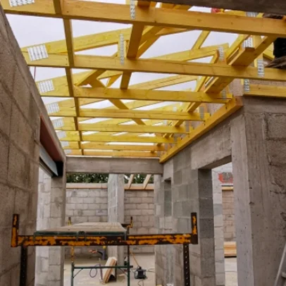 Construction de maison inachevée avec charpente en bois jaune et murs en blocs de béton.
