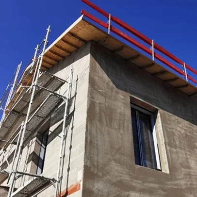 Chantier de construction: échafaudage, murs en béton, fenêtres, ciel bleu clair.